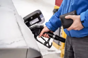 Man holding fuel nozzle, filling gas tank of diesel car covered with snow.