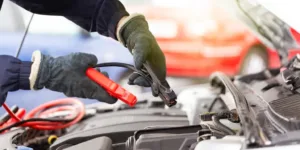 man with gloves jump starting car with jumper cables